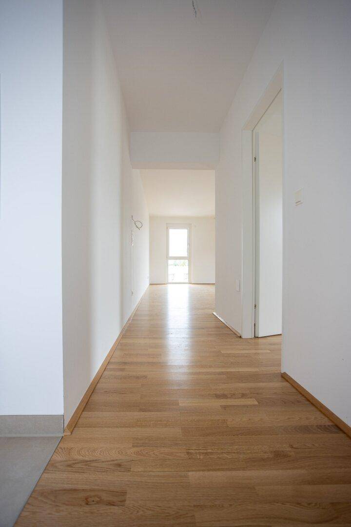 Heller Flur mit Parkettboden, der zu weiteren Räumen und einem Fenster führt.