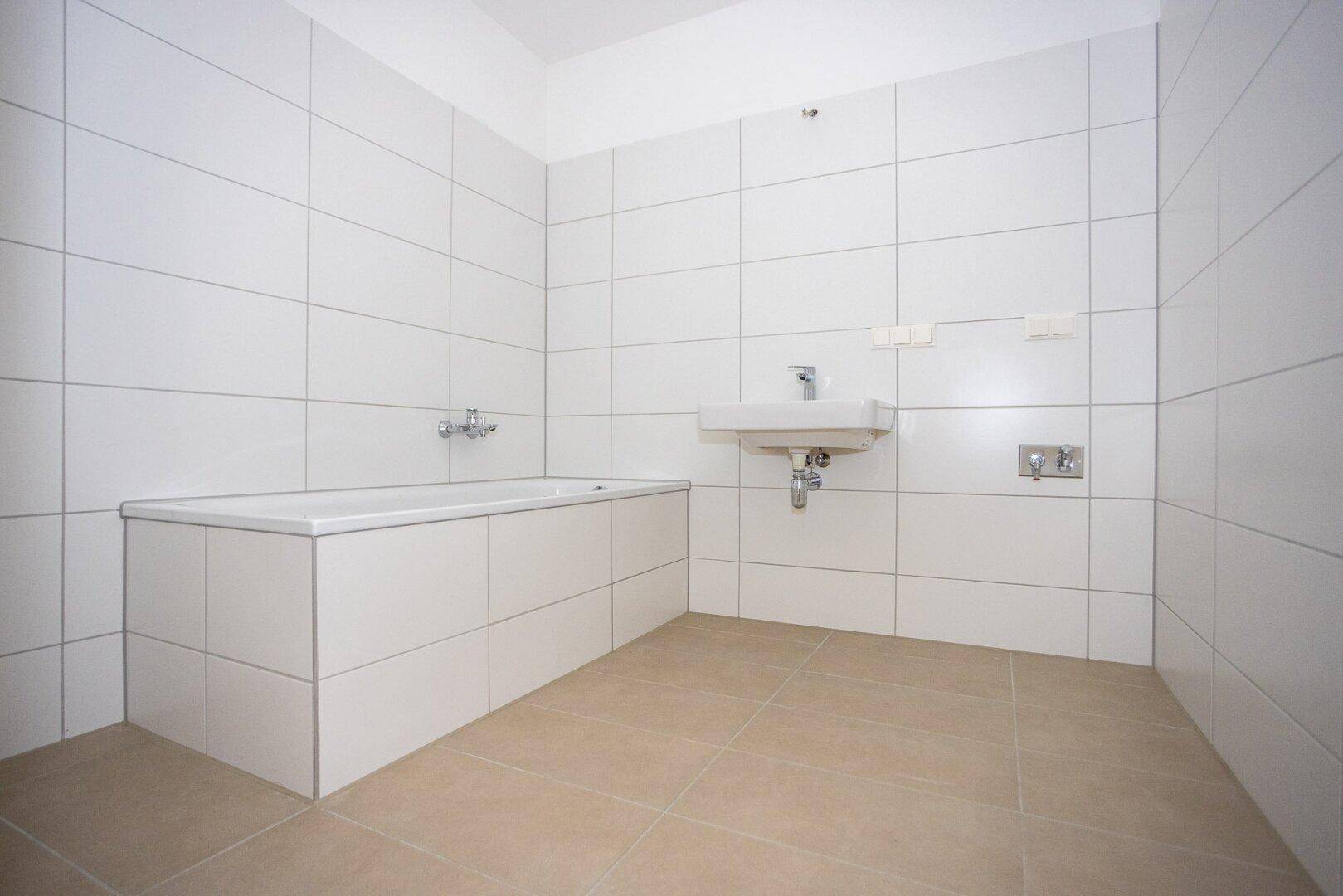 Modernes Badezimmer mit weißen Fliesen, integrierter Badewanne und Waschbecken.