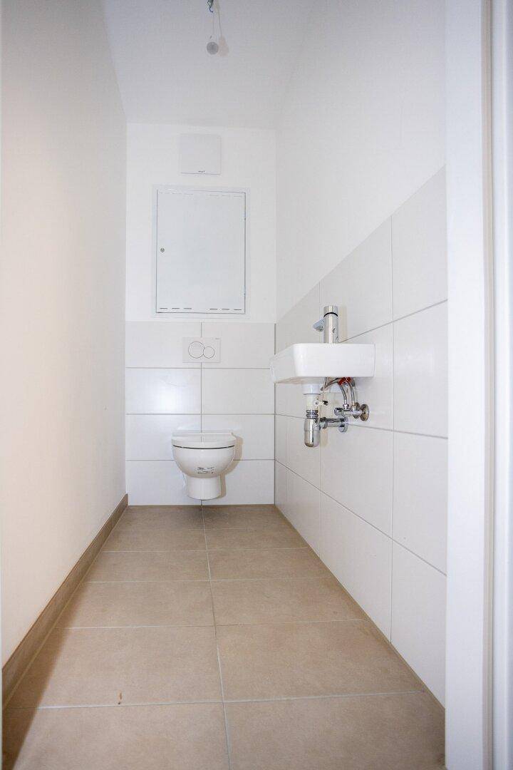 Separates Gäste-WC mit Wand-WC, kleinem Waschbecken und hellen Fliesen.