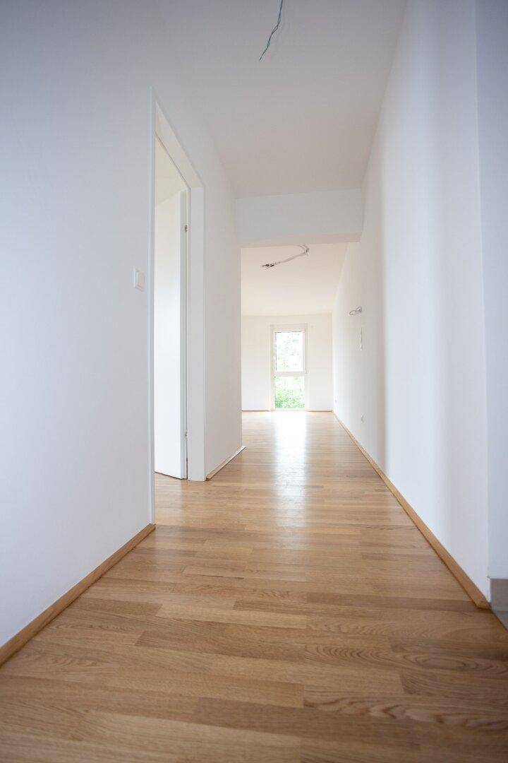 Langer, heller Flur mit Parkettboden und Blick auf ein Fenster am Ende.