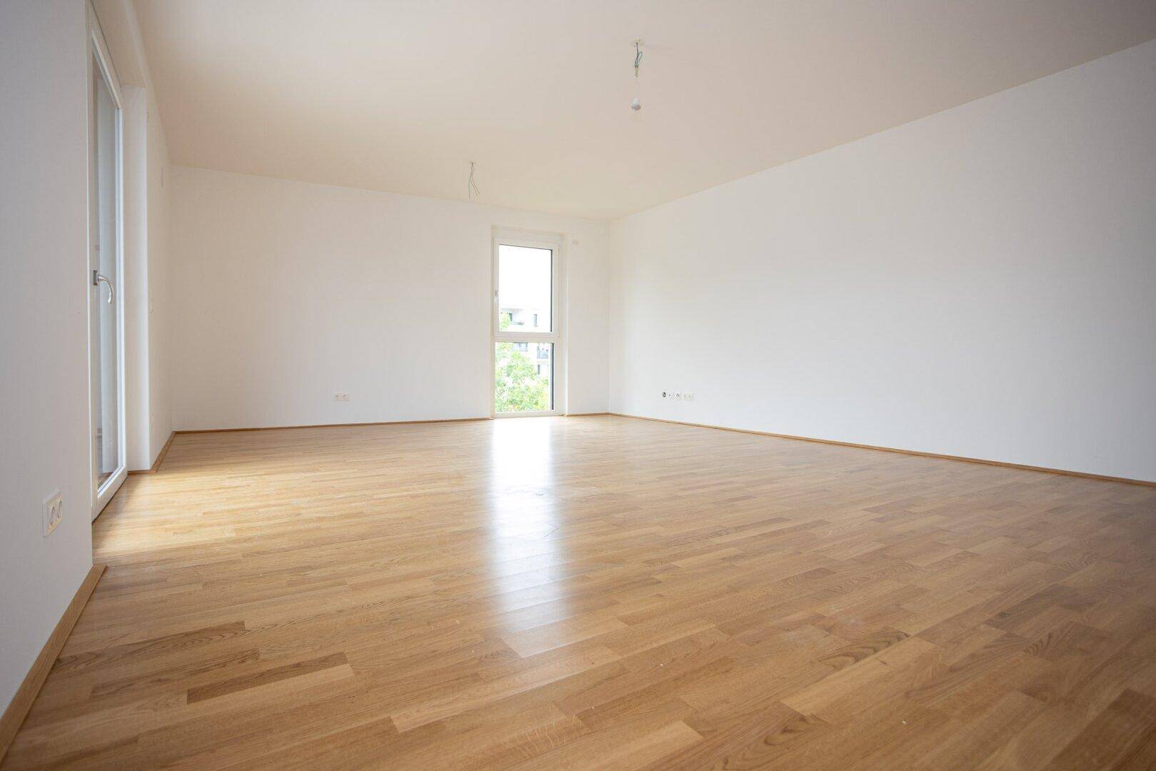 Lichtdurchfluteter Raum mit Parkettboden und großem Fenster, ideal für Wohnzwecke.