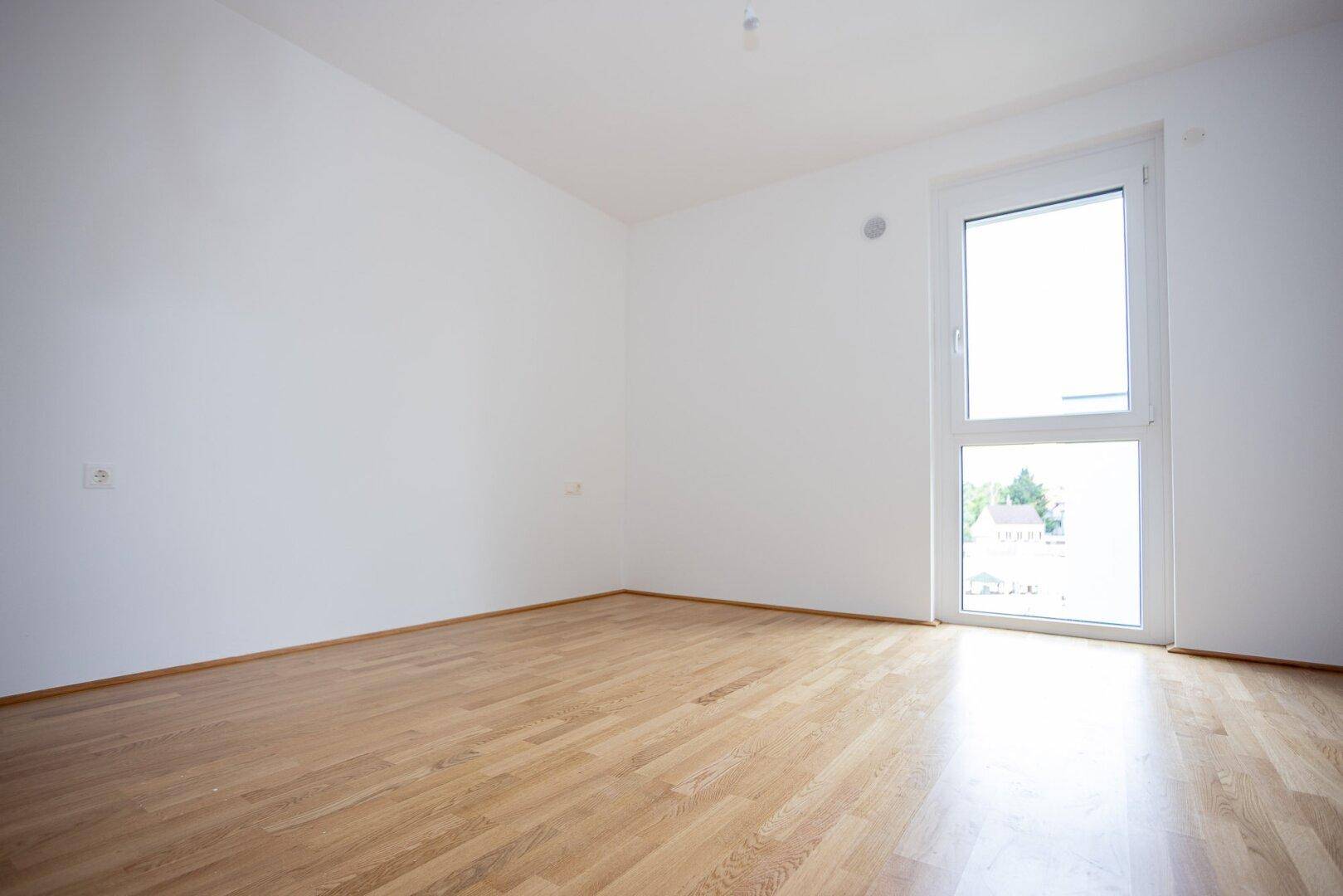 Helles Schlafzimmer mit Parkettboden und Fenster mit Blick nach draußen.