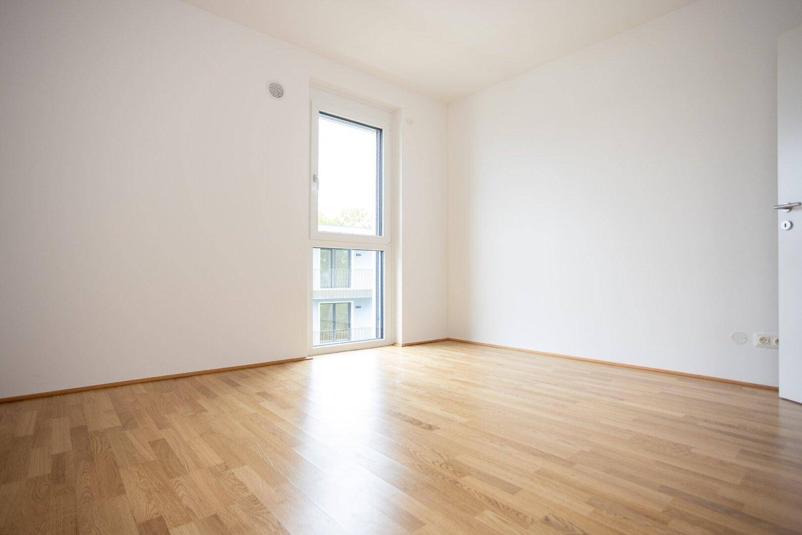 Heller Raum mit Parkettboden und hohem Fenster, ideal als Schlafzimmer oder Büro.