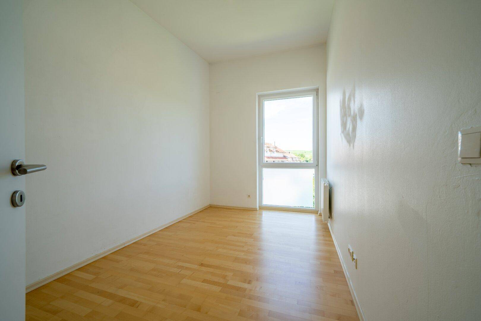 Helles Schlafzimmer mit Parkettboden und einem großen Fenster, das viel Licht spendet.