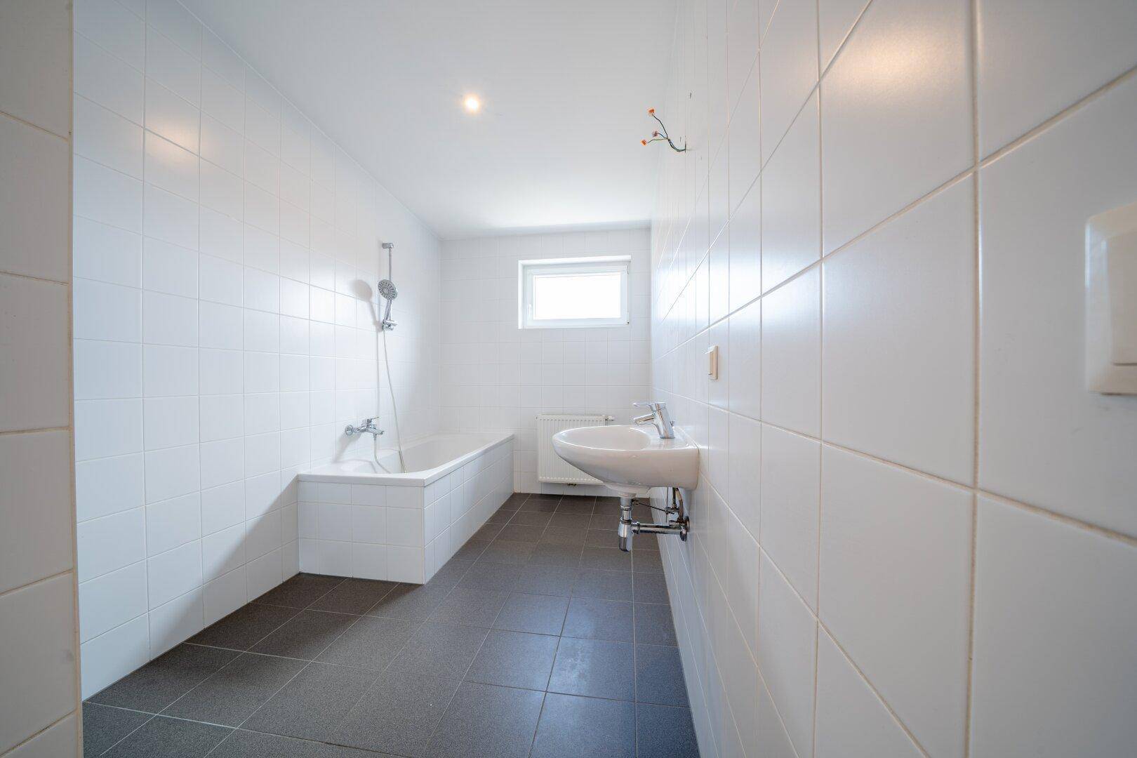 Modernes Badezimmer mit Badewanne, Waschbecken und weißen Fliesen an den Wänden.