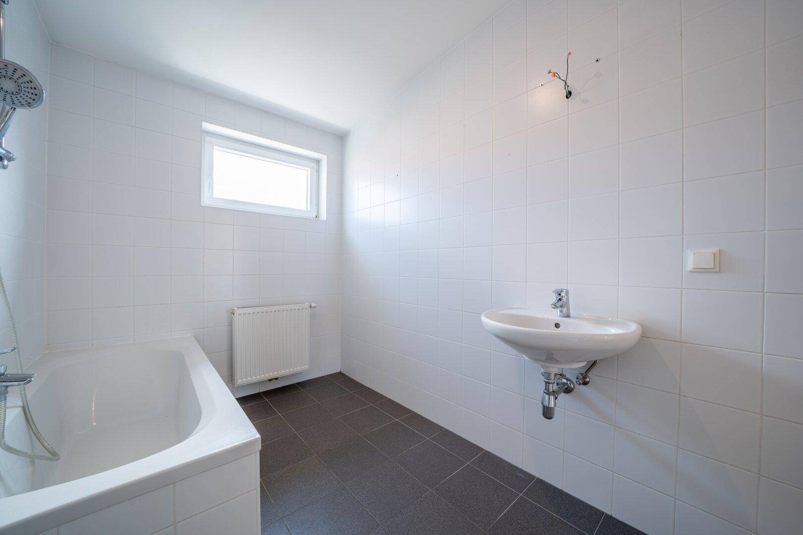 Helles Badezimmer mit Badewanne, Waschbecken und Fenster für natürliche Belüftung.