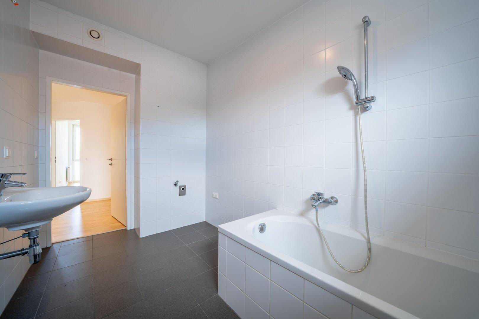 Badezimmer mit Badewanne, Waschbecken und Blick auf den angrenzenden Raum.