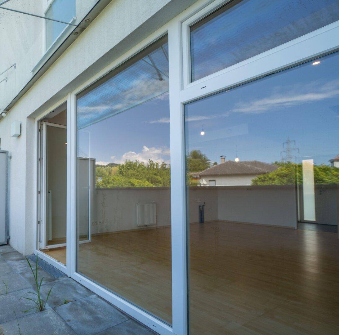 Große Fensterfront mit Blick auf die Umgebung und Zugang zu einer Außenterrasse.