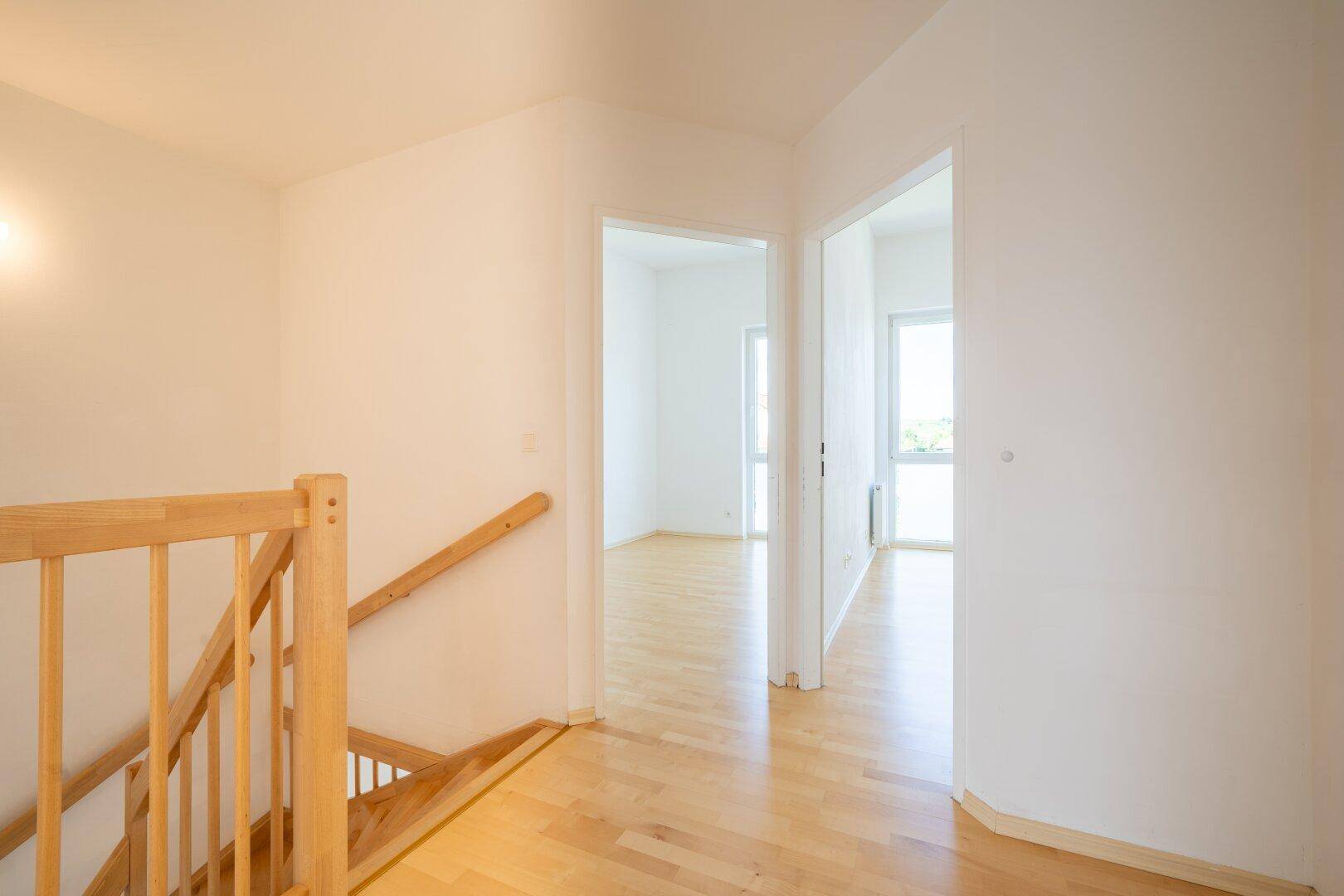Heller Flur im Obergeschoss mit Holztreppe und Zugang zu weiteren Zimmern.