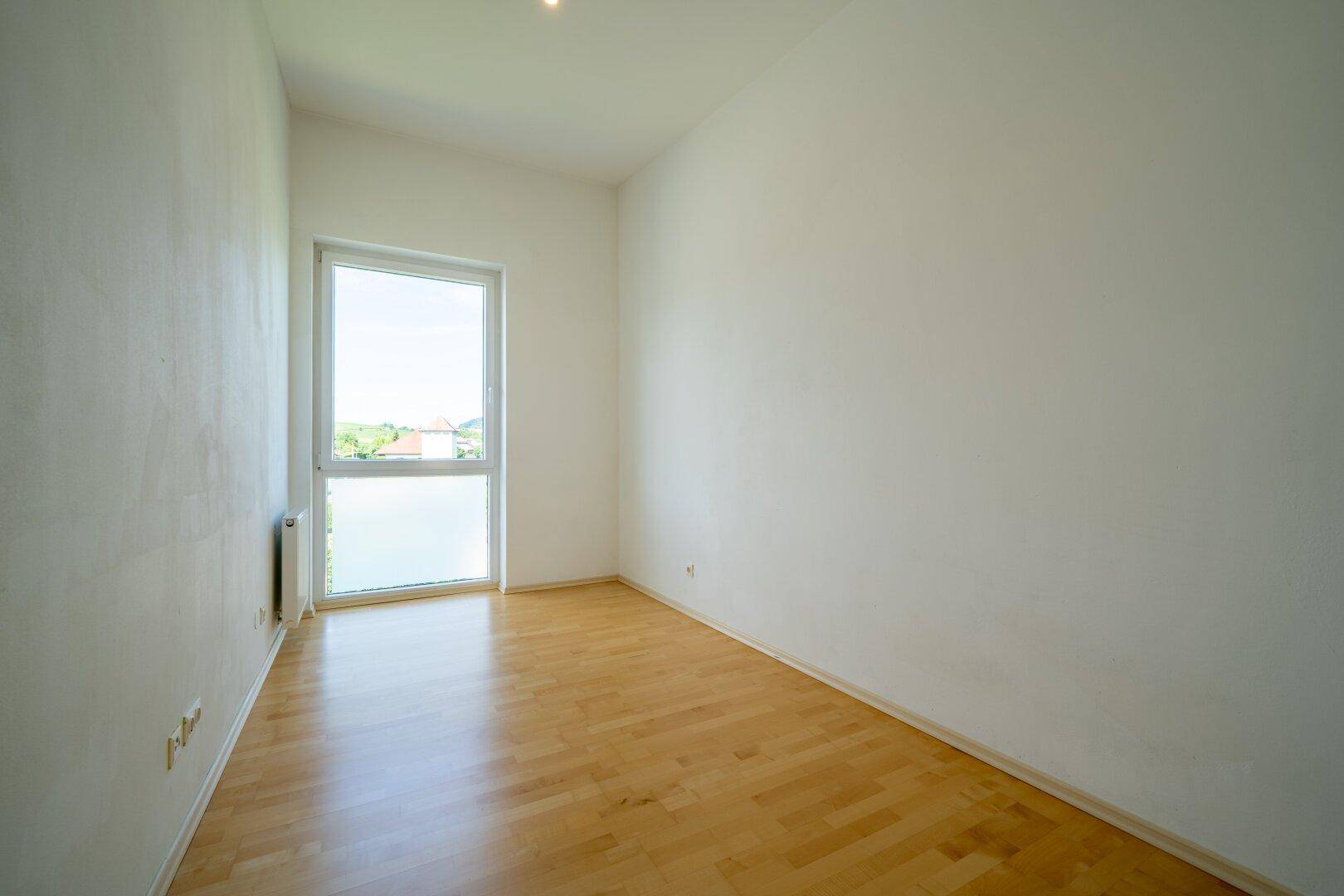 Schlafzimmer mit Parkettboden und Fenster, das einen Blick nach draußen ermöglicht.