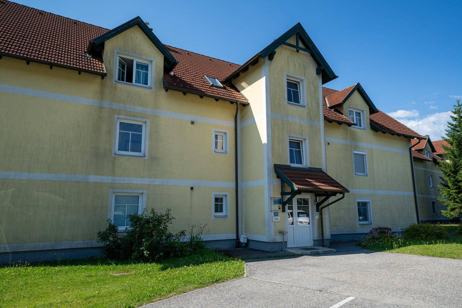 Gelbes Gebäude mit rotem Dach und Gaubenfenstern, das den Haupteingang und die Architektur zeigt.