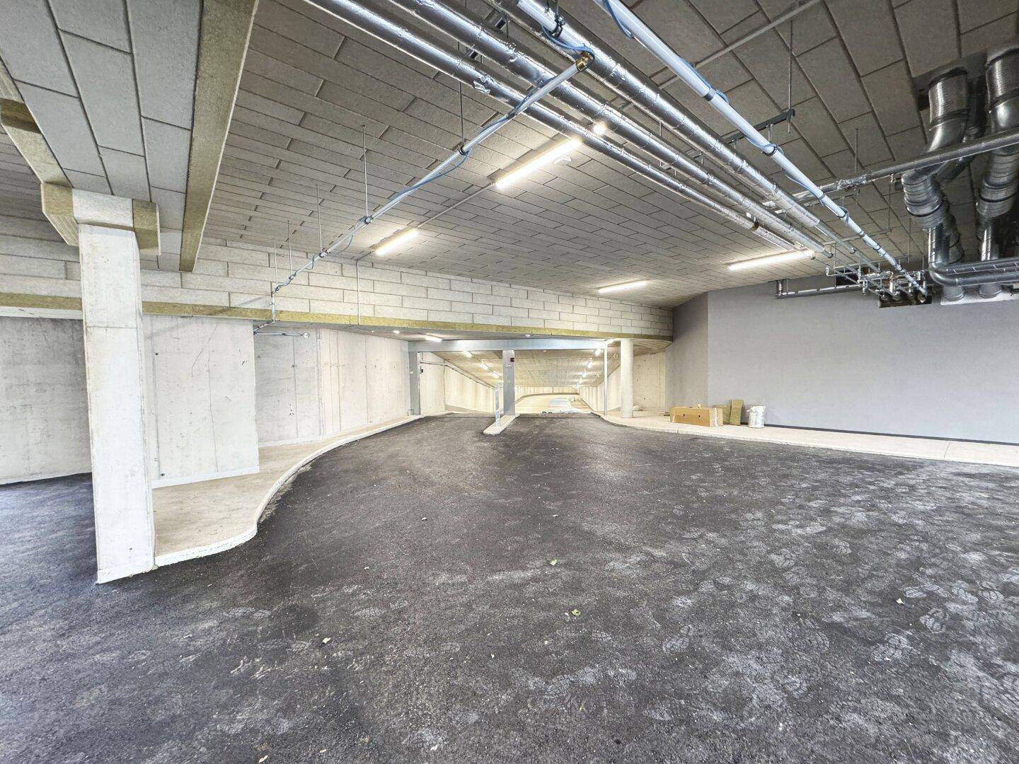 Tiefgarageneinfahrt mit Rampe und sichtbaren Installationen an der Decke.