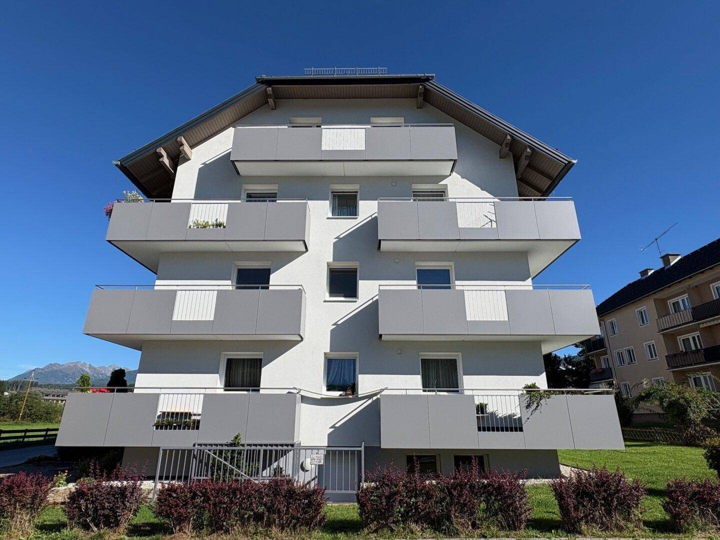 Frontansicht eines zeitgenössischen Wohnhauses mit vielen Balkonen und weitem Blick auf die Landschaft und Berge.