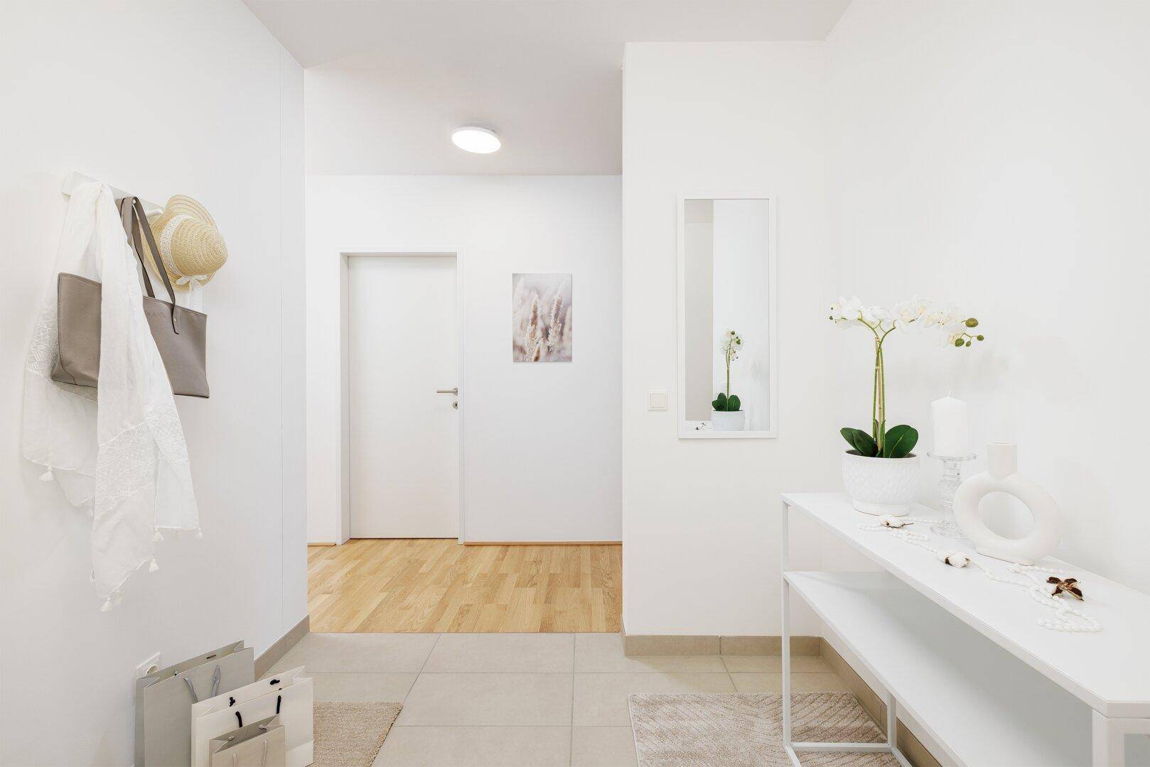 Heller Eingangsbereich mit Fliesenboden, Spiegel und Garderobe.