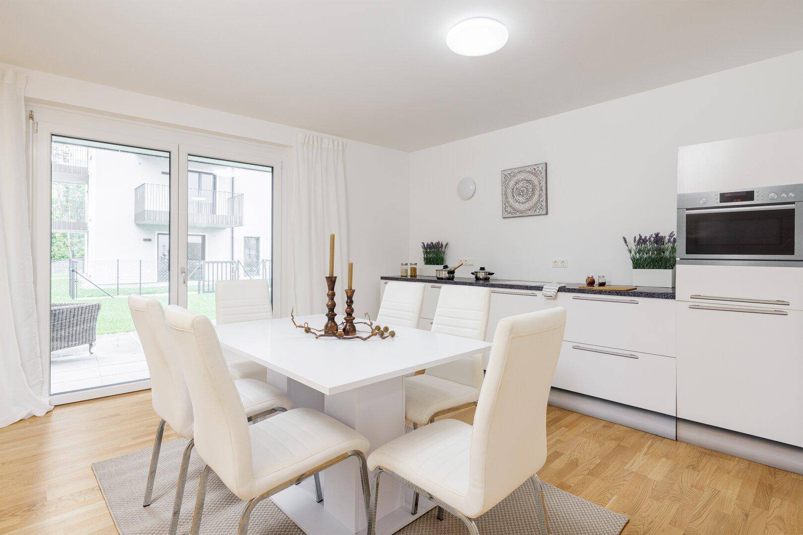 Moderner Essbereich mit weißem Tisch und integrierter Küche im Hintergrund.