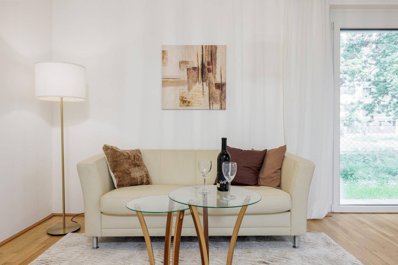Detailansicht des Wohnbereichs mit beigem Sofa, Couchtisch und großem Fenster.