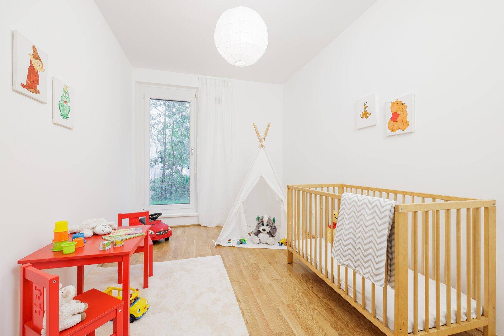 Freundliches Kinderzimmer mit Babybett, Spieltisch und Holzboden.