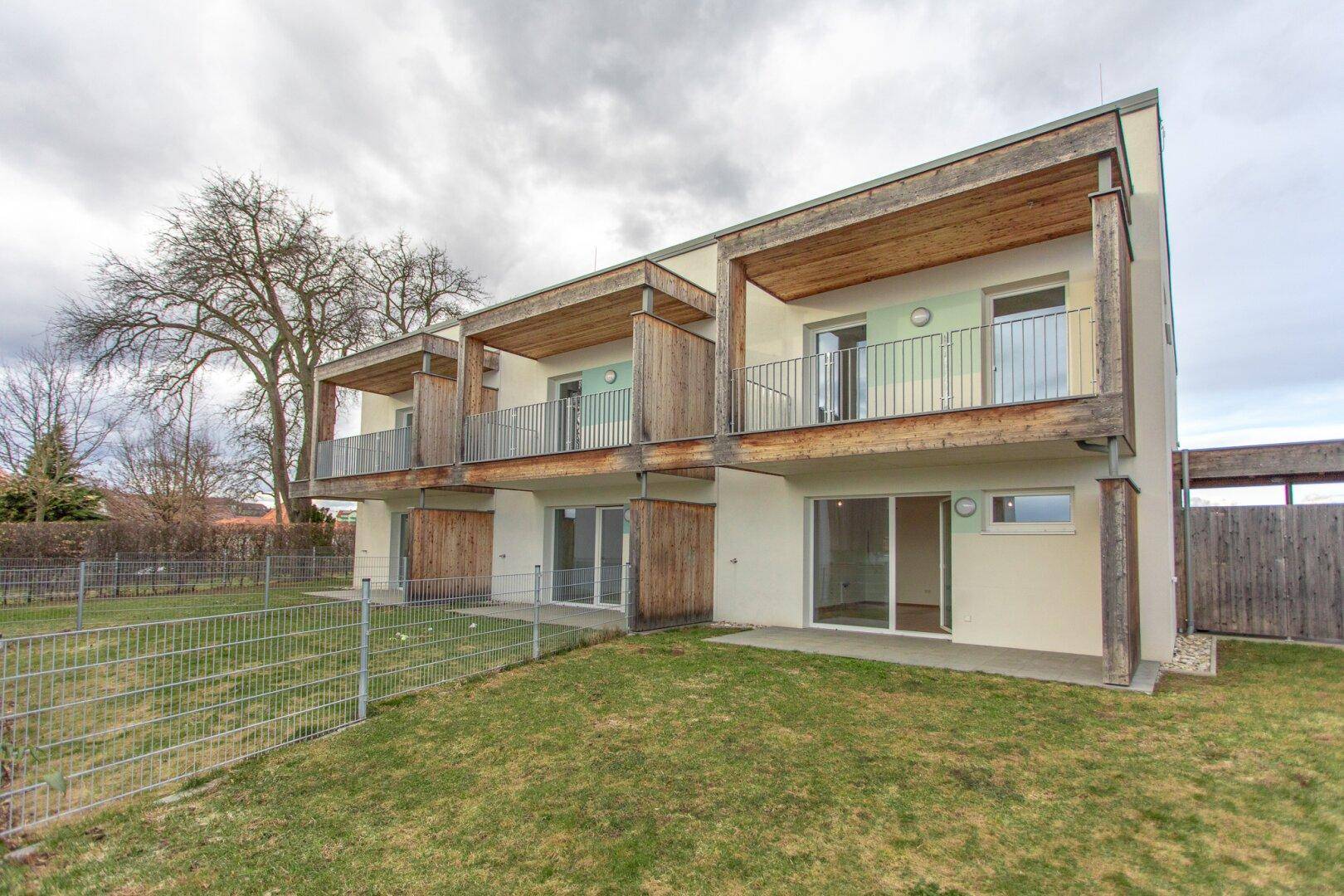 Rückseite eines modernen Gebäudes mit Holzverkleidung, Balkonen und privatem Gartenbereich.