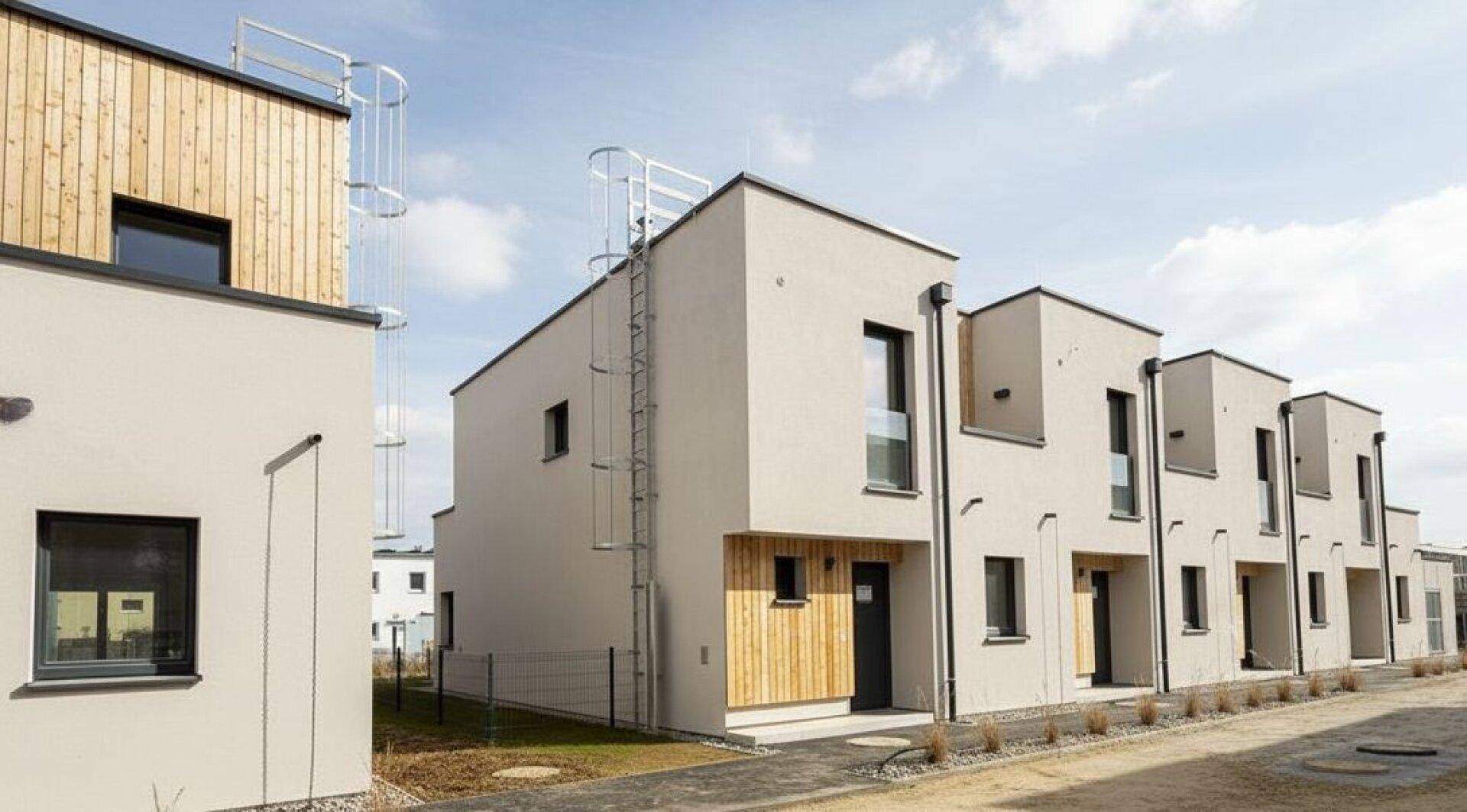Moderne Reihenhäuser mit heller Fassade und Holzverkleidung unter blauem Himmel.