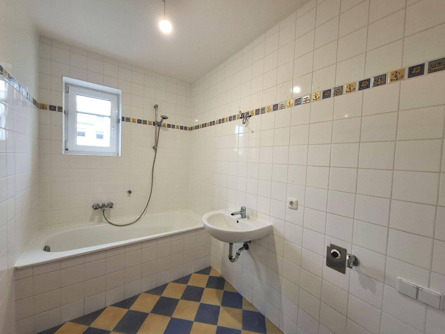Badezimmer mit Badewanne, Waschbecken und farbigen Fliesen, inklusive Fenster für natürliche Belüftung.