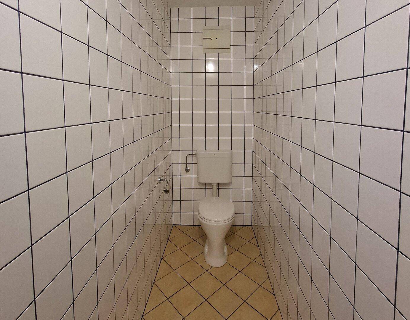Separate Toilette mit weißen Wandfliesen und beigem Boden, schlicht und funktional gestaltet.