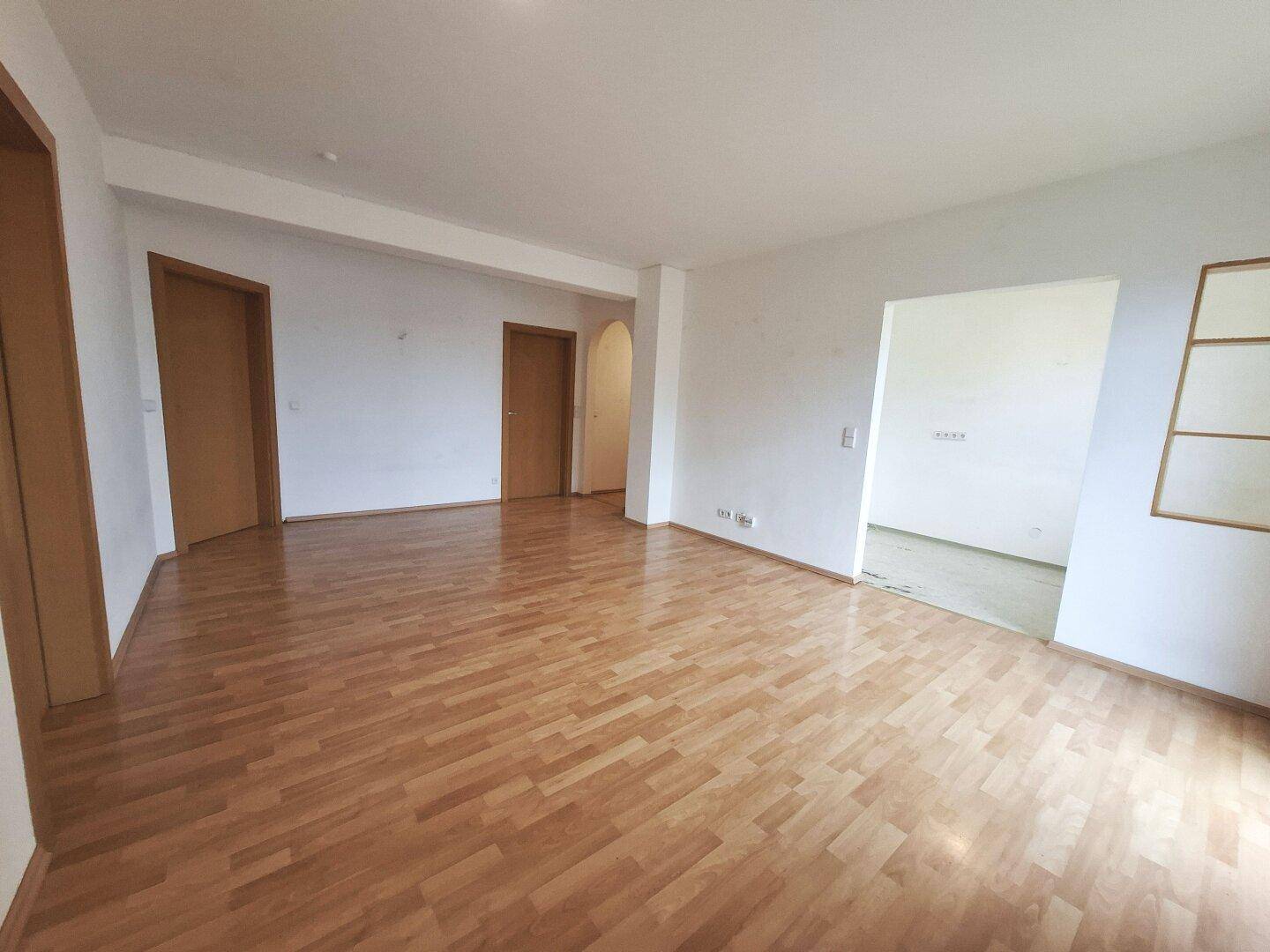 Leeres Wohnzimmer mit Laminatboden und mehreren Türen, bereit zur individuellen Gestaltung und Einrichtung.