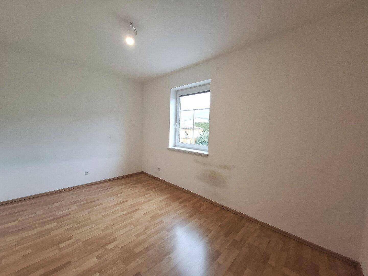 Helles Schlafzimmer mit Laminatboden und einem Fenster mit Blick ins Grüne, gut belichtet.