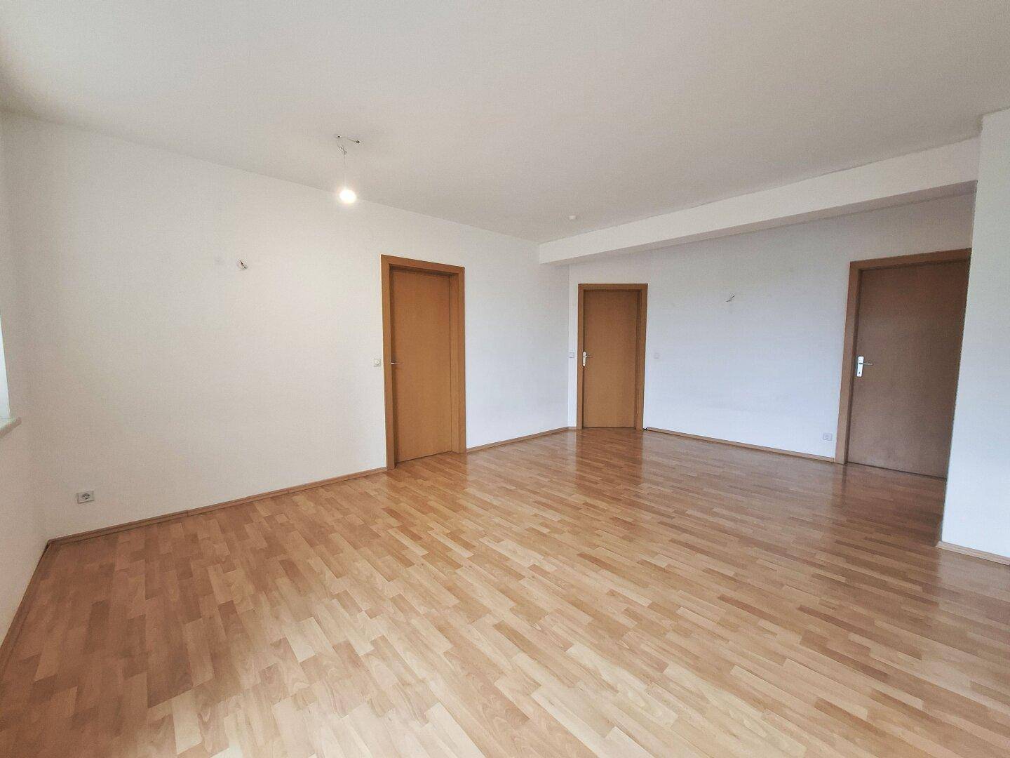 Geräumiges Wohnzimmer mit Laminatboden und einfacher Deckenbeleuchtung, hell und einladend.