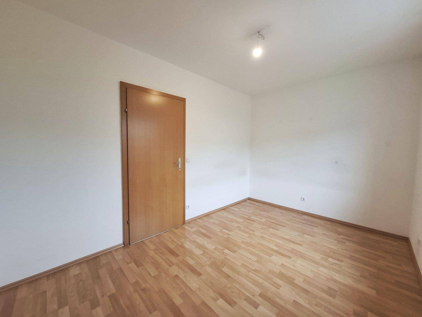 Einfaches Schlafzimmer mit Laminatboden und einer Holztür, bereit zur persönlichen Gestaltung.