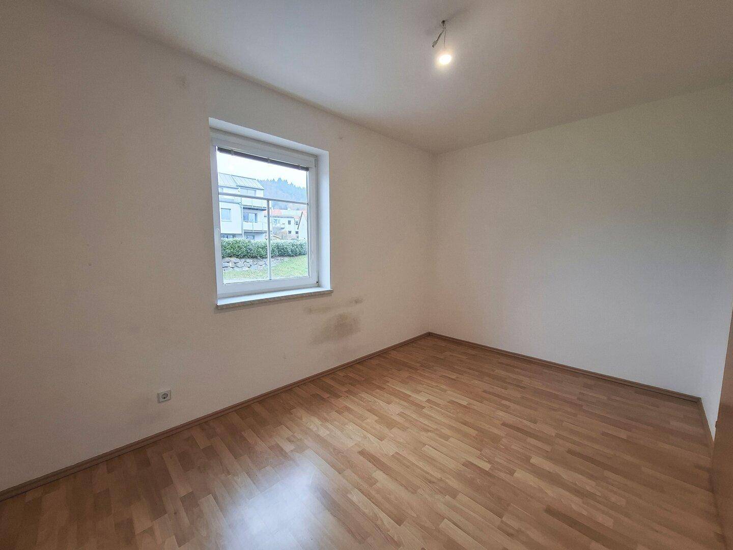 Schlafzimmer mit Laminatboden und Fenster, das viel Tageslicht in den Raum lässt und eine grüne Aussicht bietet.