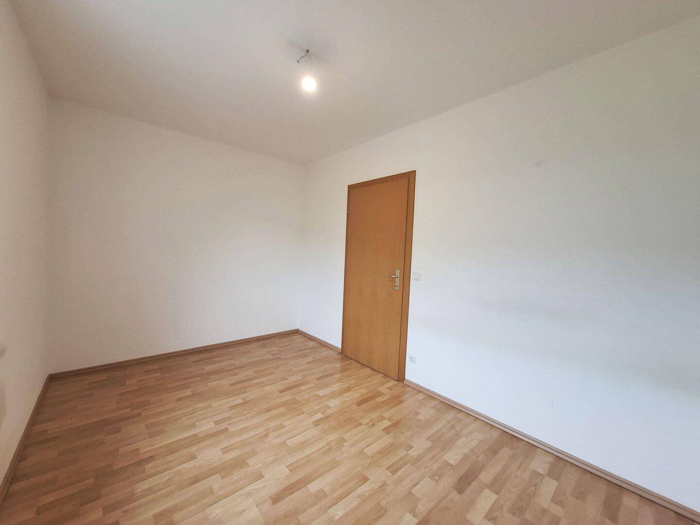 Leeres Schlafzimmer mit Laminatboden und schlichten weißen Wänden, ideal für individuelle Einrichtung.
