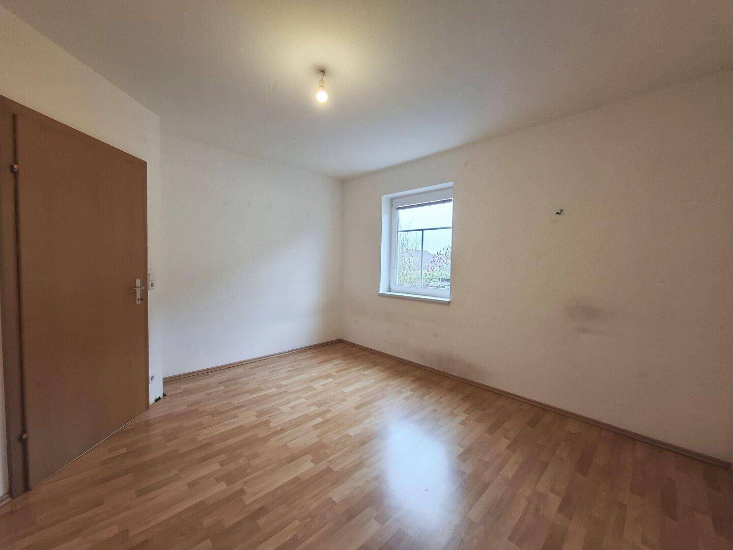 Schlafzimmer mit Laminatboden und einer Holztür, schlicht und funktional gestaltet, bereit zur Nutzung.