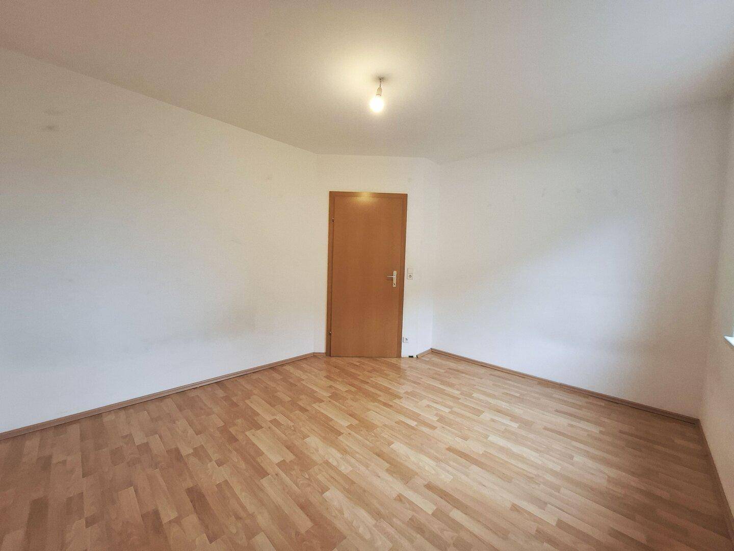 Leeres Schlafzimmer mit Laminatboden und einer Holztür, bereit für neue Bewohner und individuelle Gestaltung.