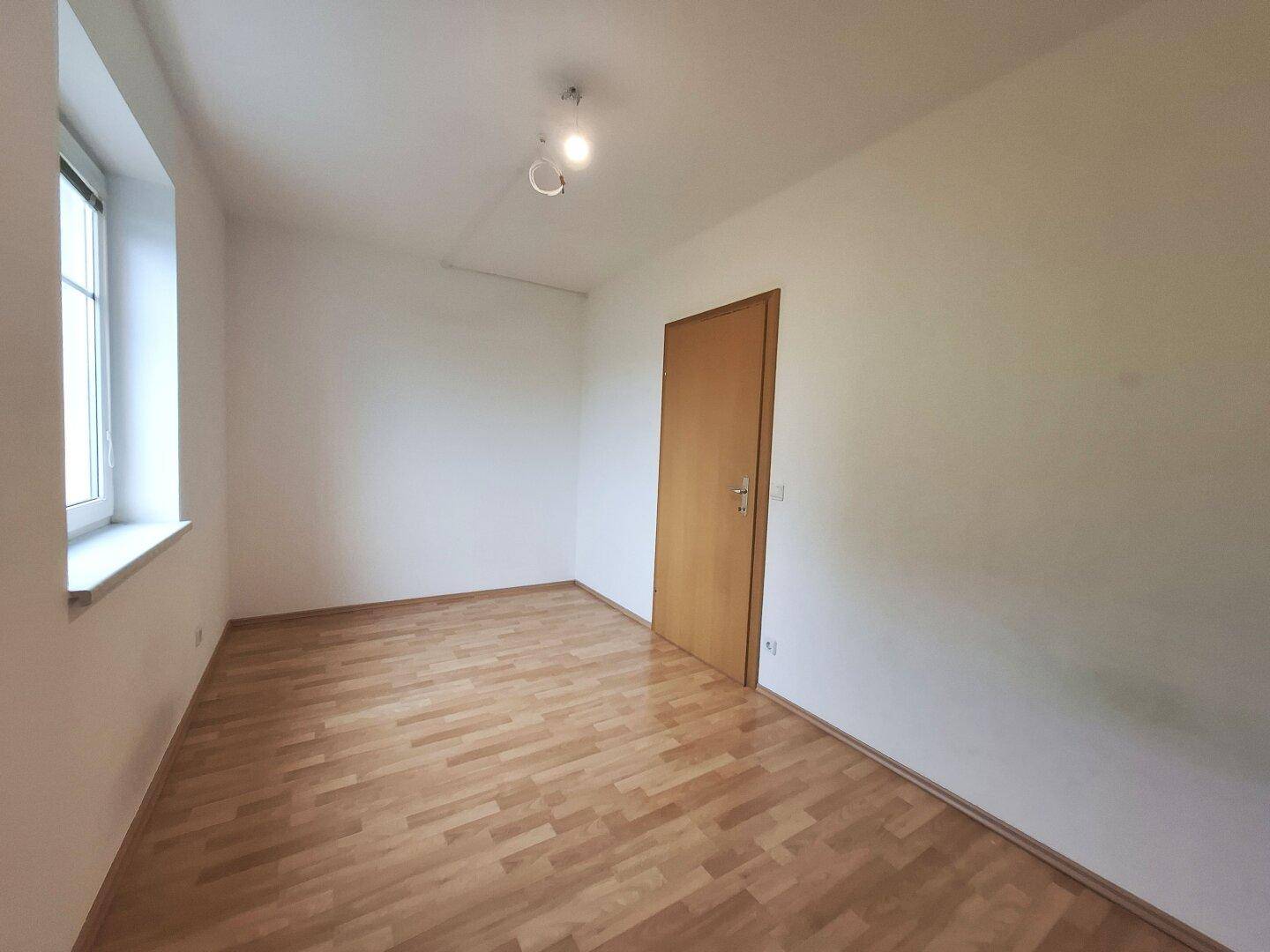 Helles Schlafzimmer mit Laminatboden und einem Fenster, das den Raum mit Tageslicht füllt und eine angenehme Atmosphäre schafft.