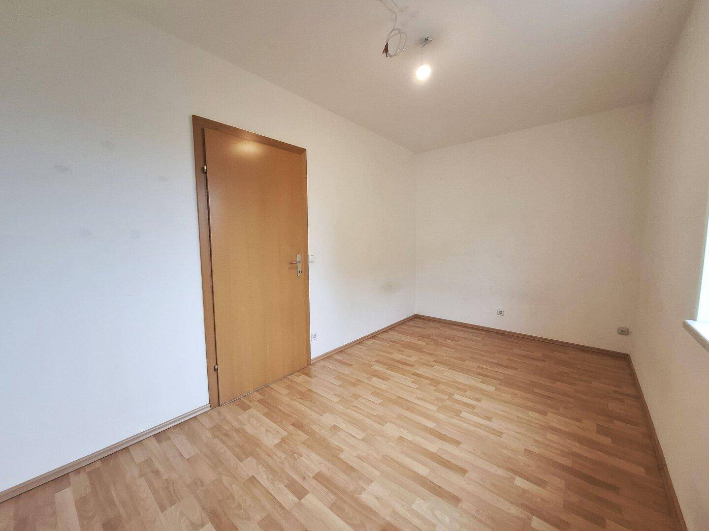 Schlafzimmer mit Laminatboden und einer Holztür, die den Raum vom Flur trennt und Privatsphäre bietet.