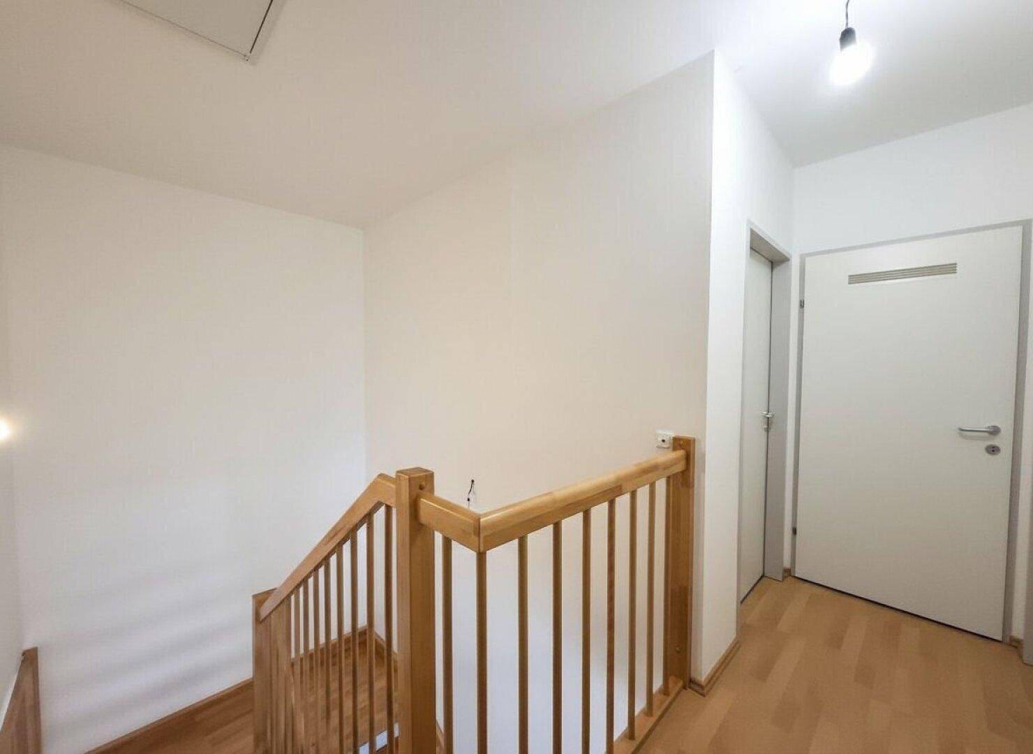 Heller Flur im Obergeschoss mit Holztreppe und Zugang zu weiteren Räumen.