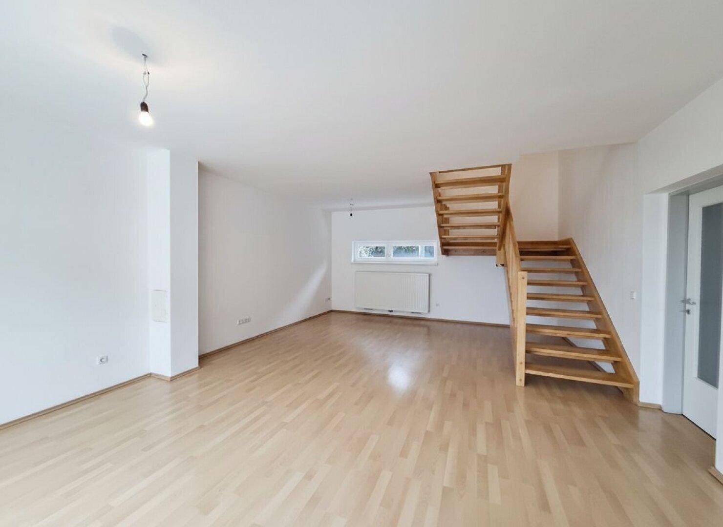 Heller Wohnraum mit Holztreppe und Parkettboden, bietet viel Platz für individuelle Einrichtungsideen.