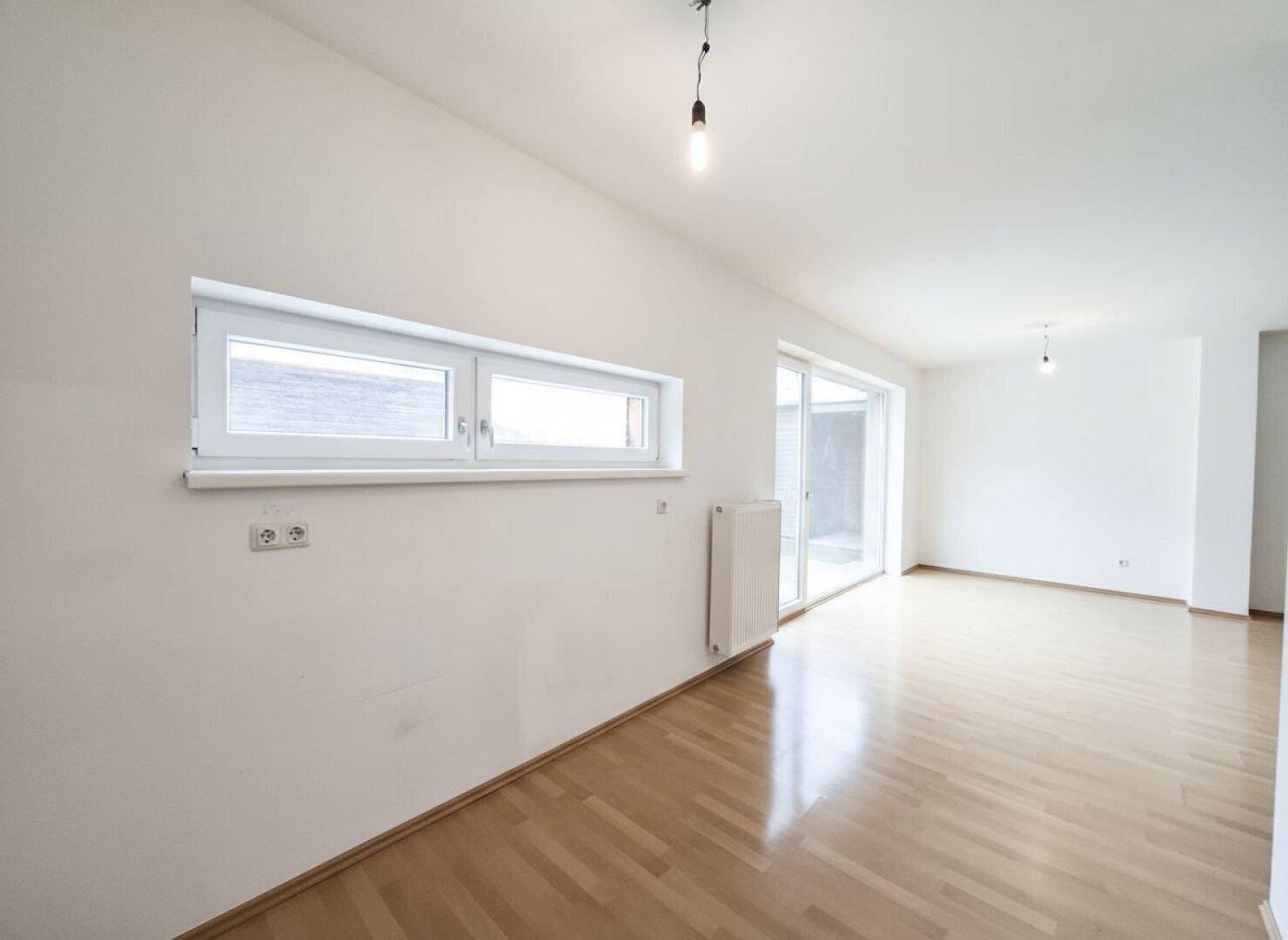 Lichtdurchfluteter Wohnbereich mit großen Fenstern und Zugang zu einem Außenbereich.