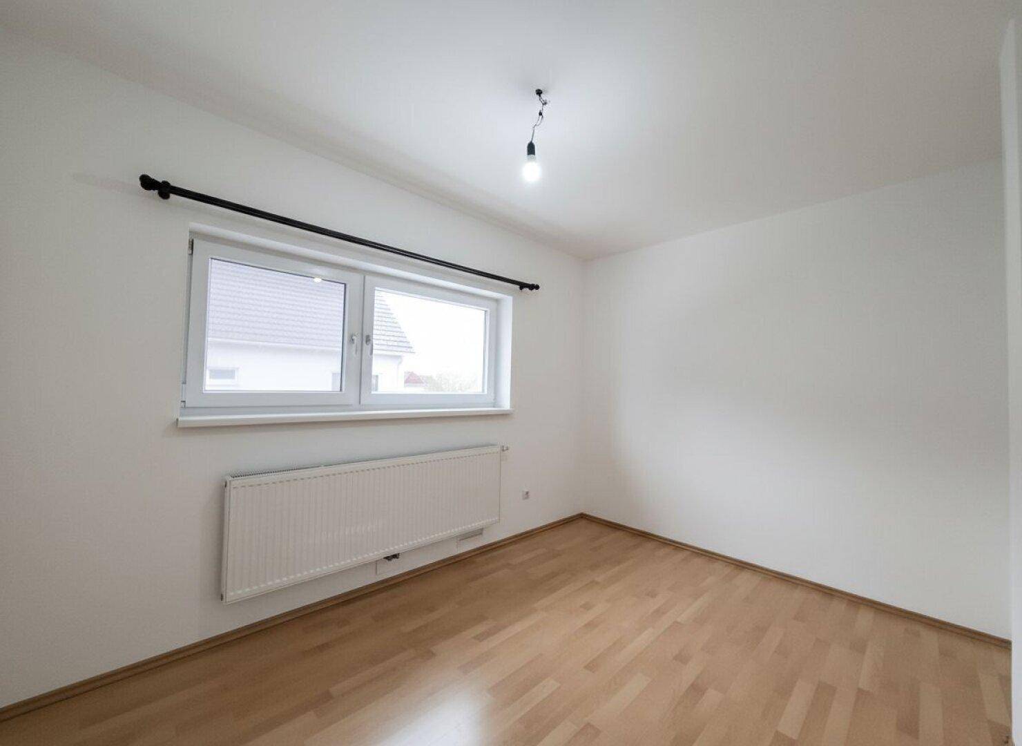 Helles Zimmer mit Parkettboden und großem Fenster, ideal für ein Kinder- oder Gästezimmer.