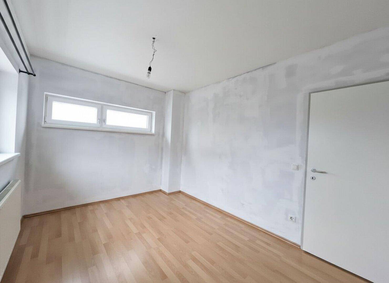 Geräumiges Zimmer mit Parkettboden und einem Fenster, ideal als Schlaf- oder Arbeitszimmer.