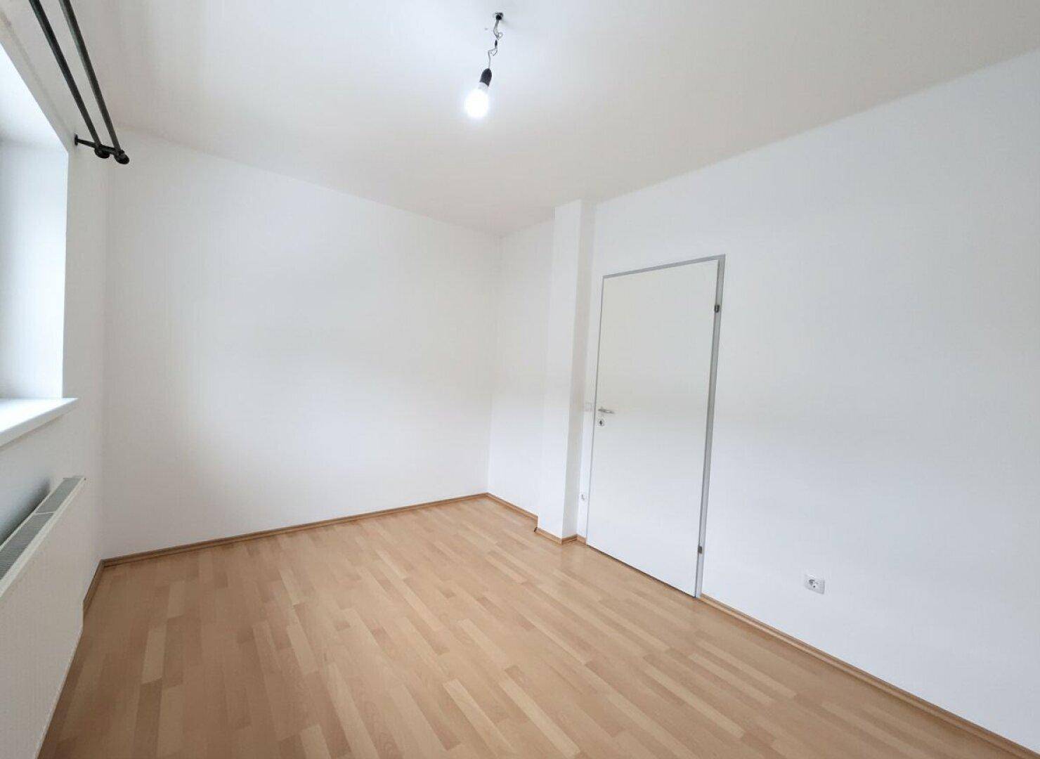 Geräumiges Zimmer mit Parkettboden und Fenster, bietet eine angenehme Wohnatmosphäre.