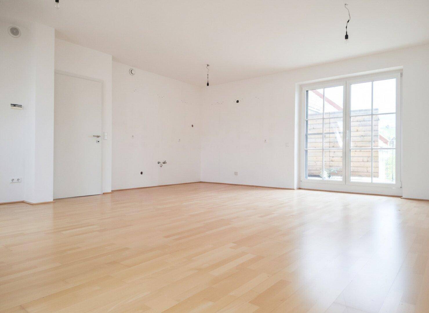 Heller Wohnbereich mit Parkettboden und einer großen Balkontür, bereit zur individuellen Gestaltung.