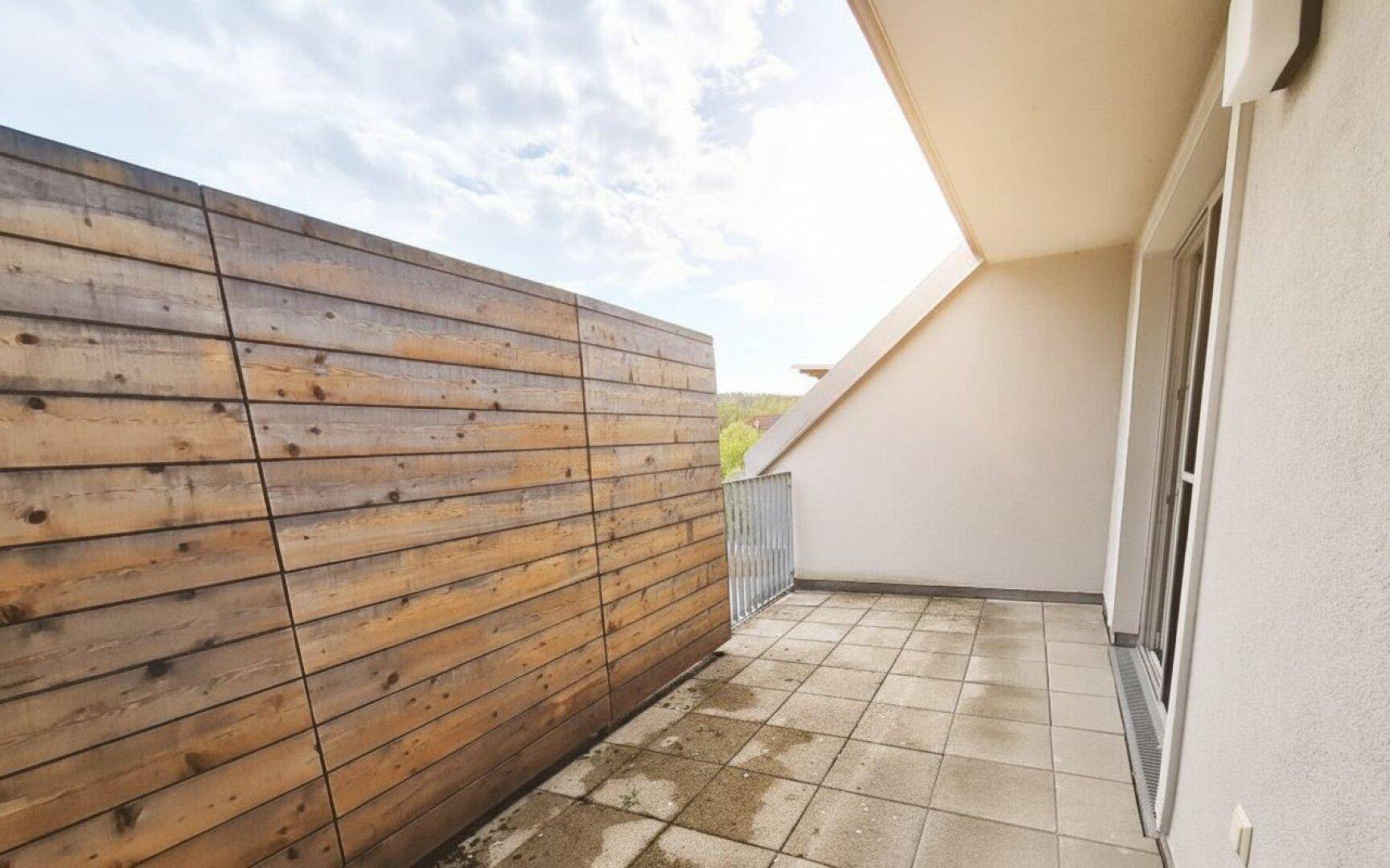 Geräumiger Balkon mit Holzwand als Sichtschutz und Fliesenboden, ideal für Entspannung im Freien.