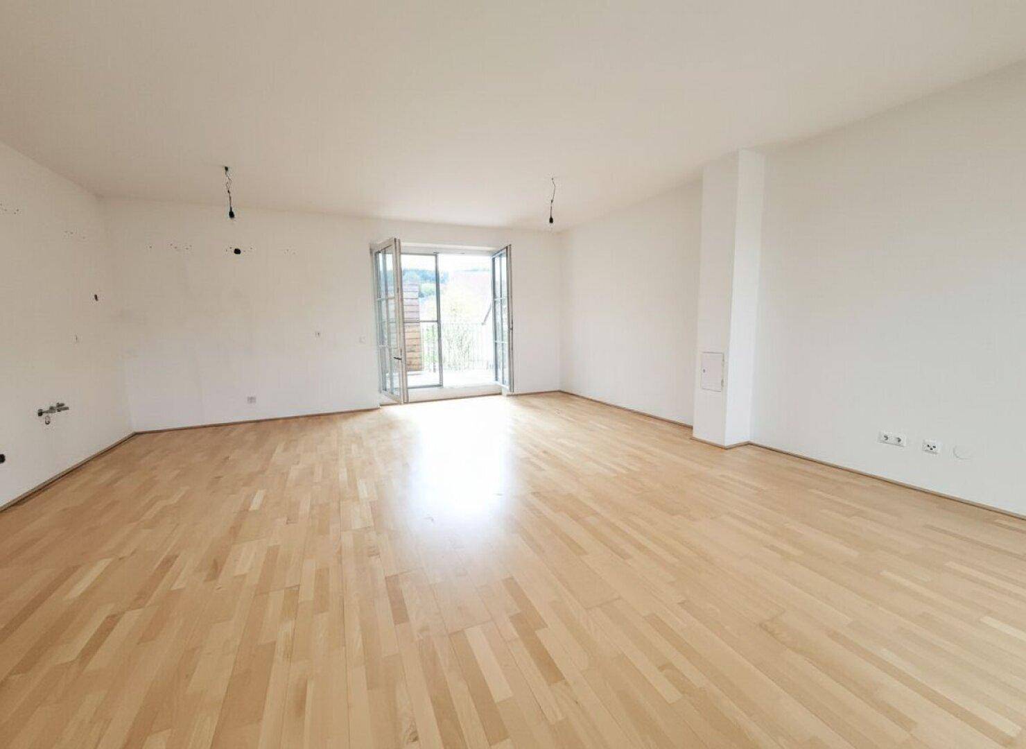 Lichtdurchfluteter Wohnraum mit Parkettboden und direktem Zugang zum Außenbereich durch eine Doppeltür.