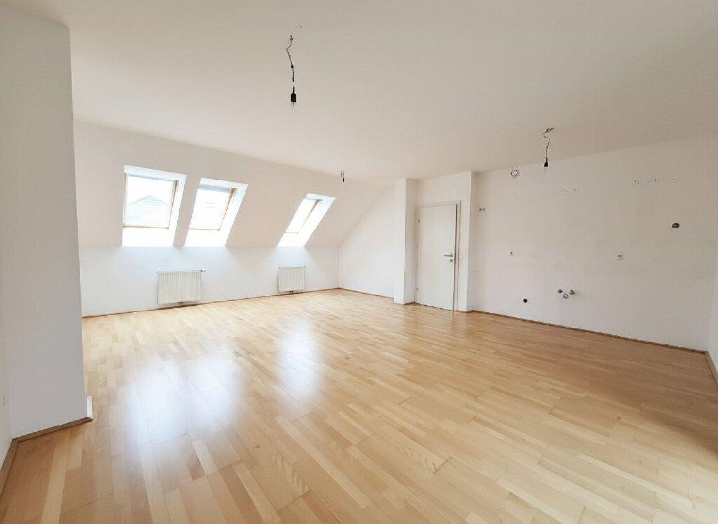 Heller Wohnbereich im Dachgeschoss mit schrägen Wänden, Parkettboden und mehreren Dachfenstern.