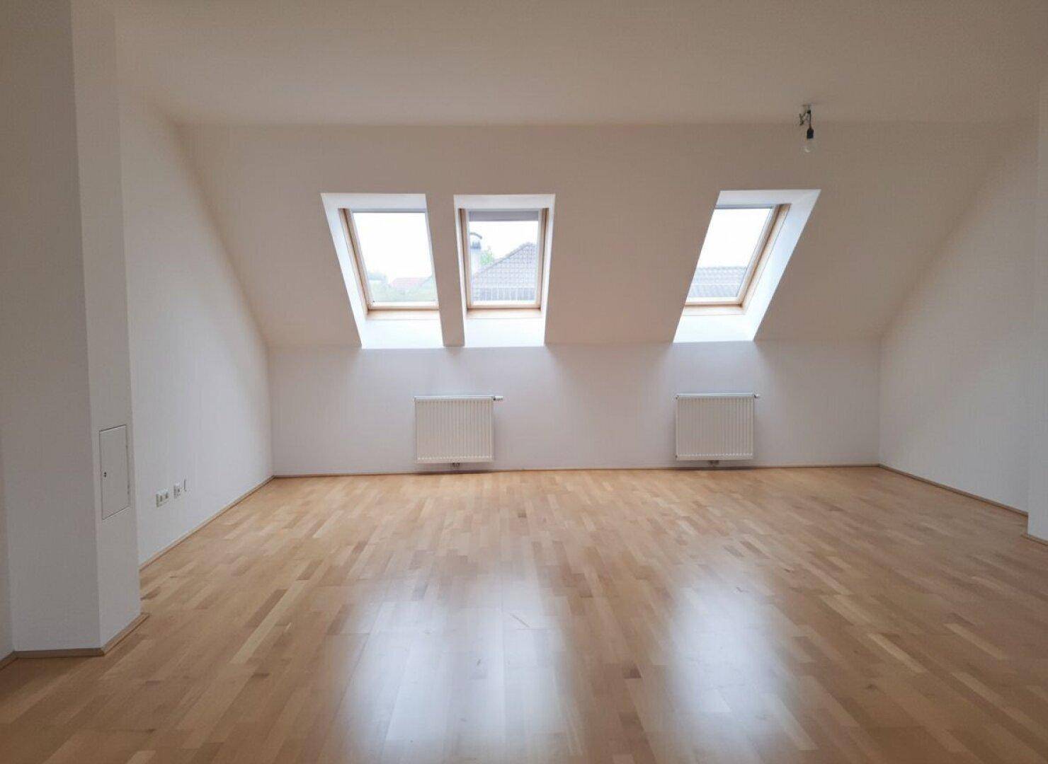 Geräumiger Dachgeschossraum mit Parkettboden und drei großen Dachfenstern, die viel Licht hereinlassen.