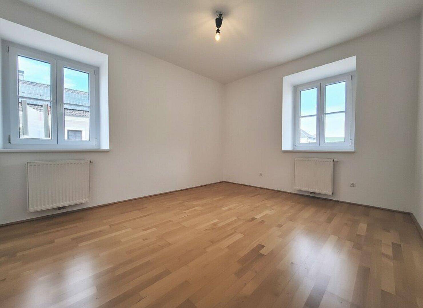 Geräumiges Schlafzimmer mit zwei Fenstern, Parkettboden und viel natürlichem Lichteinfall.