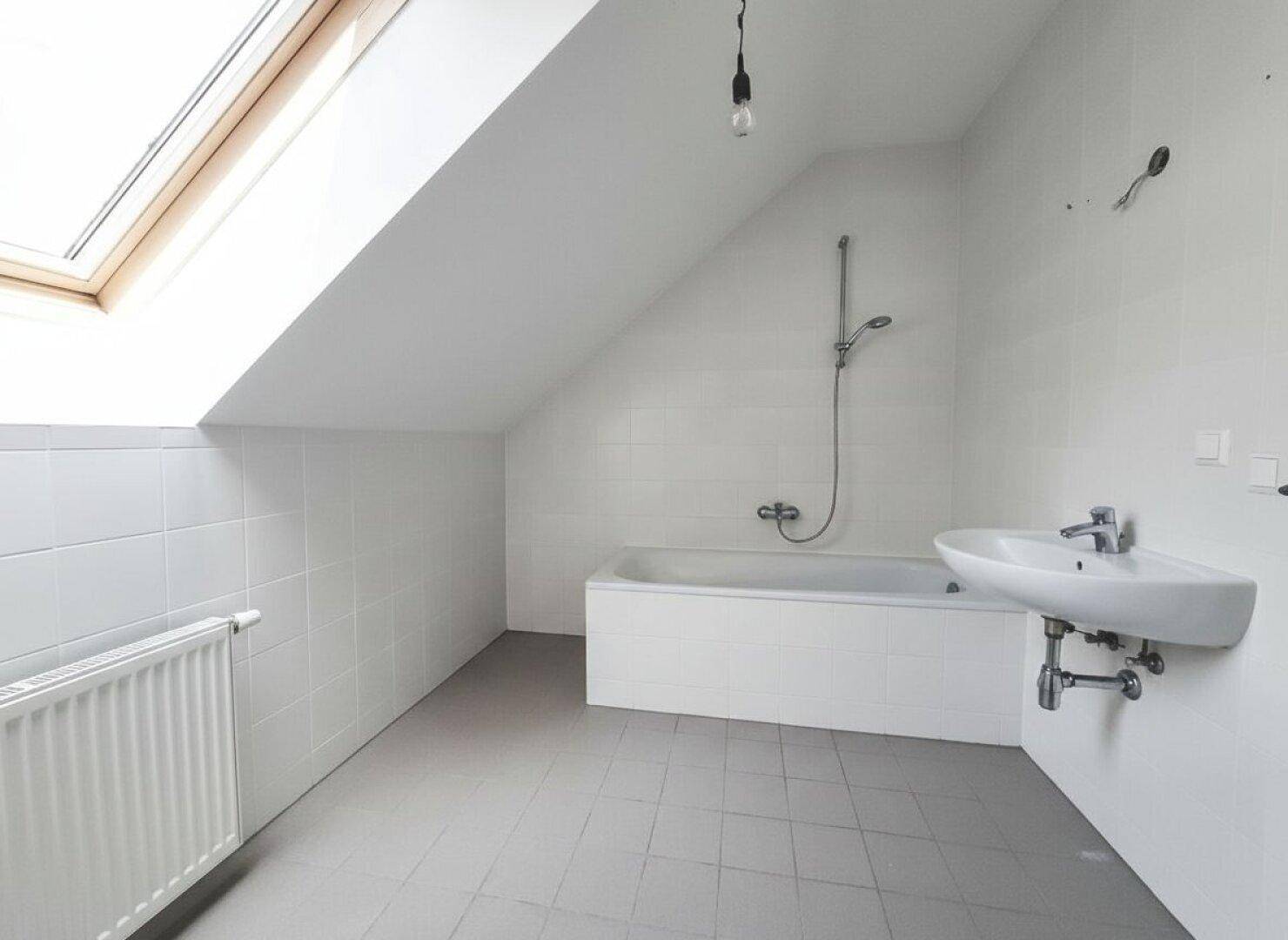 Modernes Badezimmer im Dachgeschoss mit Badewanne, Waschbecken, Fliesen und einem Dachfenster.