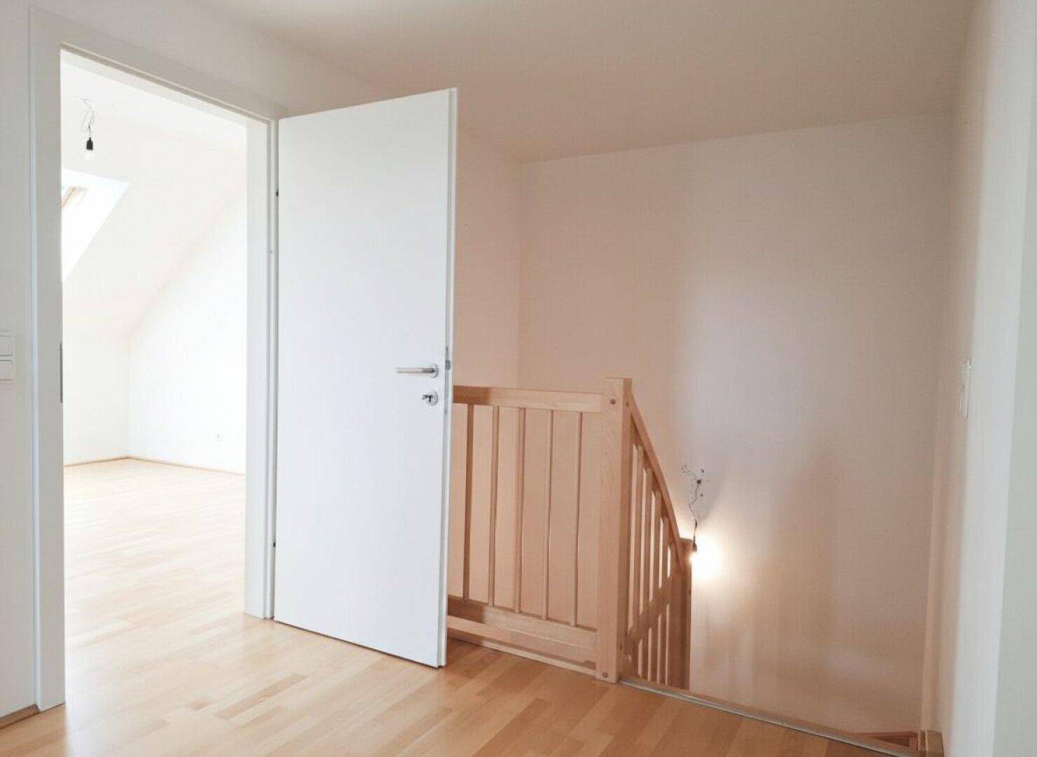 Heller Flur mit Holztreppe und Parkettboden, der zu den oberen Etagen führt.