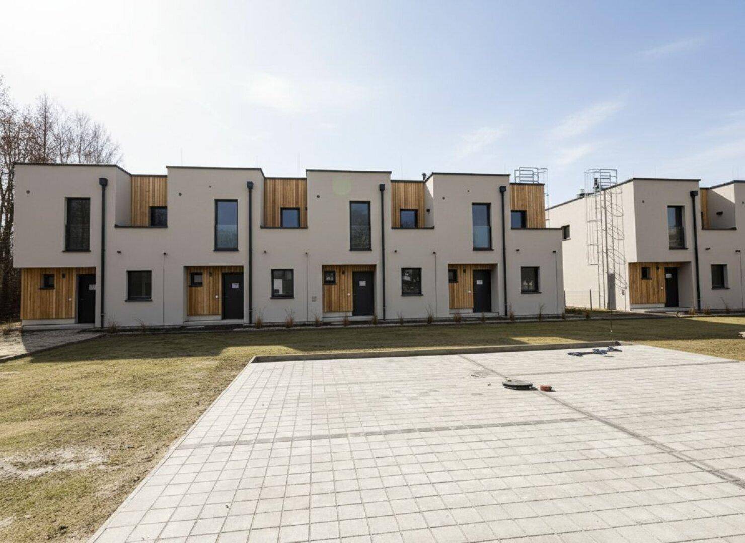 Moderne Reihenhäuser mit heller Fassade und Holzdetails, umgeben von Grünflächen und Parkplätzen.